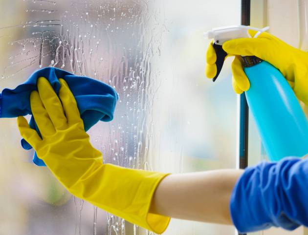 Gloved hand cleaning window rag and spray Female hand in yellow gloves cleaning window pane with rag and spray detergent. Cleaning concept